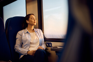 Woman with eyes closed enjoying by the window while traveling by train.