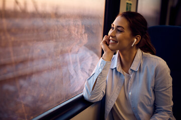 Happy woman enjoys in view through the window while traveling by train at sunset. © Drazen