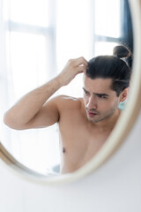 shirtless man adjusting hair bun and looking at mirror.