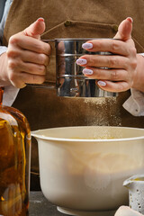The female hands of the cook are preparing a culinary product, dough, sift flour through a sieve. Shallow depth of field