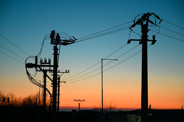 Electric poles with power lines at sunset. Electricity transmission. - obrazy, fototapety, plakaty