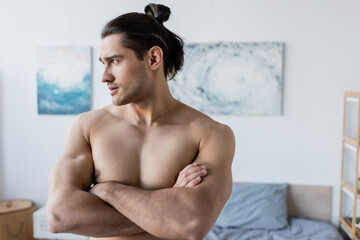 muscular man with long hair standing with crossed arms and looking away.