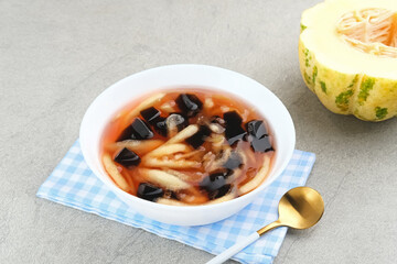 Es Blewah or contain slices of cantaloupe with grass jelly and syrup. Served in bowl on grey background.

