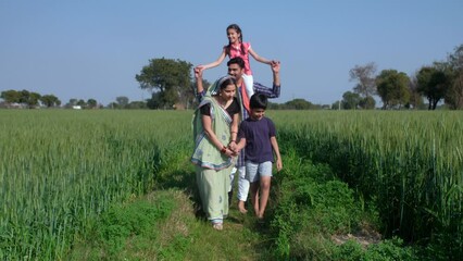 A middle-aged bearded farmer enjoys carrying his little daughter on his shoulders - happy parenting carefree father-daughter bonding. A small nuclear village family walking through their agricult... - Powered by Adobe