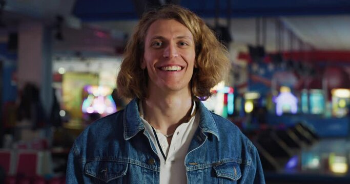 Cinematic shot of happy young blond hair male bowler is smiling in camera while having fun to play bowling with college friends on weekend in sporting club.