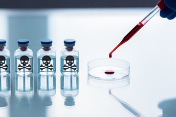 A pipette and a Petri dishes with human blood sample and a row of ampoules with a skull and bones black sign in a lab, selected focus. Prohibited development of warfare.