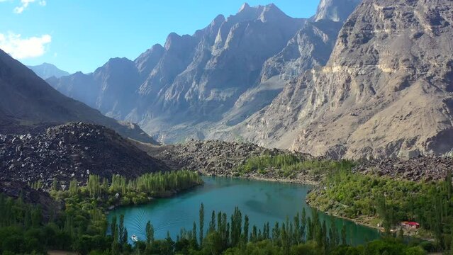 Aerial view of turquoise blue water at upper kachura lake surrounded by forest in skardu pakistan on a sunny day with a beautiful large mountain range in the distance