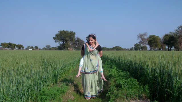 A happy village lady in traditional Saree carrying her little daughter on her back - mother-daughter bonding  piggyback. A little girl spending time with her mother roaming in an open field - a hap...