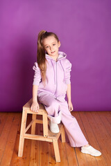 A beautiful little girl in a purple suit on a purple background. Childhood, joy, emotions