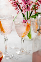 Pink cocktail with orange slice and ice cubes in crystal glasses with pink spring flowers Hyacinth. Alcoholic, refreshing party drink.