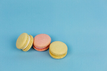 Multicolored macaroons on a plain blue background are the place for the inscription. Small French pastries. Orange and yellow macaroons. Sweets.