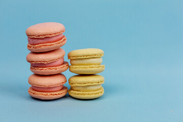 Towers of macaroni cakes in yellow and pink pastel tones on a blue background. culinary concept. Delicious multicolored macaroons.
