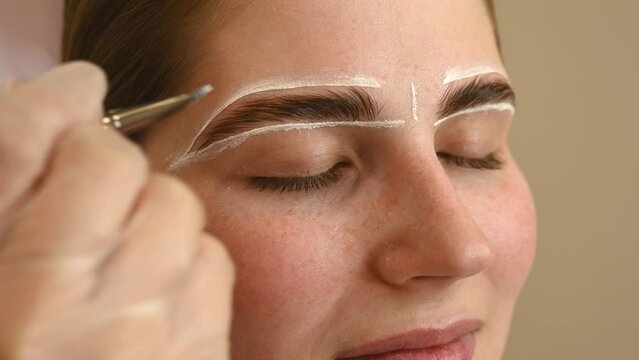 The master draws the shape of the eyebrows with white paint before coloring. 
