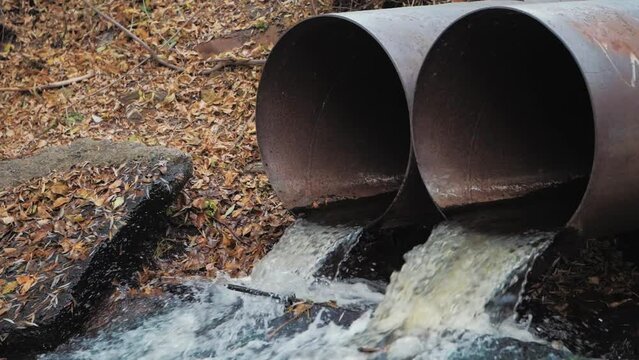 Environment protection concept. Industrial pipe discharging dirty waste. Runoff of excess water from the reservoir through metal pipes. Toxic waste in drain pipes.