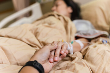 Obraz na płótnie Canvas Husband hand holding his wife hand on bed in hospital room.