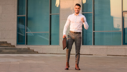 Successful lucky arabic indian business man boss leader candidate entrepreneur with briefcase standing in city near modern building wins achive gets opportunity new job makes victory gesture