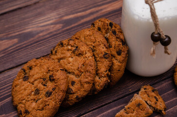 Bottle of fresh milk with homemade cookies with chocolate and raisins on a wooden table
