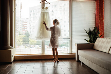 morning of the bride, the bride stands near the window with her wedding dress
