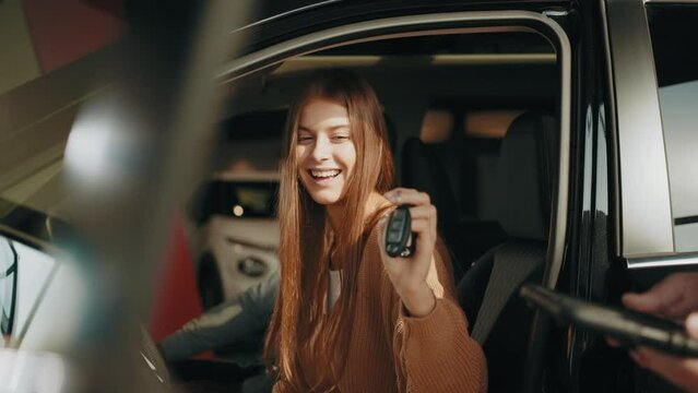 Car dealer giving key to new car owner. Woman receiving car keys from a dealer. Choosing of new vehicle. Concept of expensive purchase. Happy woman taking car key from dealer in auto show or salon.