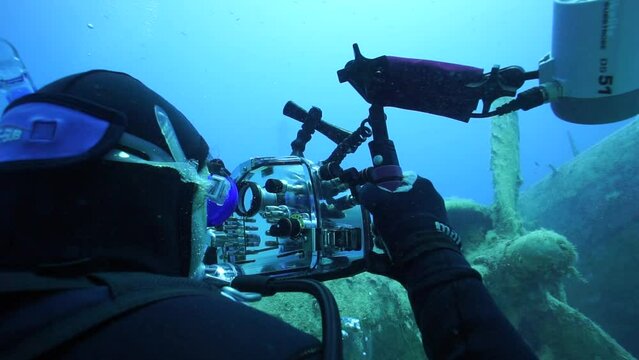 The image of the diver taking the photo of the sunken ship under the sea with a flash.