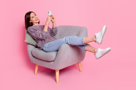 Portrait of attractive cheerful girl in armchair using device gadget smm isolated over pink pastel color background