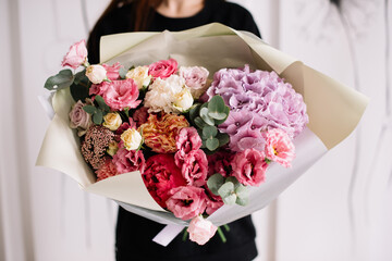 Very nice young woman holding big and beautiful bouquet of fresh hydrangea, roses, eustoma, carnations, eucalyptus in pink and purple colors, cropped photo, bouquet close up