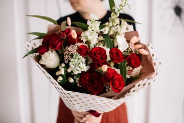 Fototapeten Very nice young woman holding big and beautiful bouquet of fresh roses, delphinium, bruin, eucalyptus in red and white colors, cropped photo, bouquet close up © anastasianess
