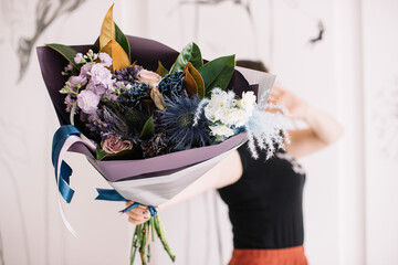 Very nice young woman holding big and beautiful exotic bouquet of fresh palm, matthiola, roses, delphinium, in purple and blue colors, cropped photo, bouquet close up