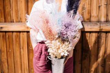 Woman holding three bunches of pink wine and purple dried flowers on the wooden wall background, close up view