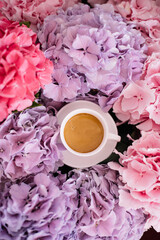 Delicious fresh morning espresso coffee with a beautiful thick crema among blossoming pink and purple hydrangea flowers at the florist shop, top view - 497292778