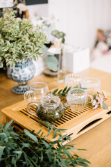 Delicious freshly brewed green tea ceremony. Glass tea cups with transparent glass tea pot standing on the wooden tray, decorated with small flowers 