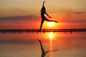 silhouette of a young slim woman in a swimsuit who dancing at sunset on the sea. summer holiday