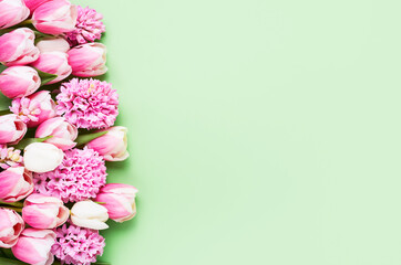 Fototapeta na wymiar Border of pink hyacinths and tulips on green backdrop. Mothers Day, Valentines Day, birthday concept