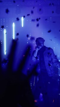 Vertical Footage of Rock Band Performing at a Concert in a Night Club. Front Row Crowd is Partying. Silhouettes of Fans Raise Hands in Front of Bright Colorful Strobing Lights on Stage.