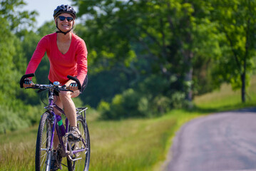 Closeup of happy woman wearing bike helmet looking aside biking on a country road on a spring summer day with copy space.