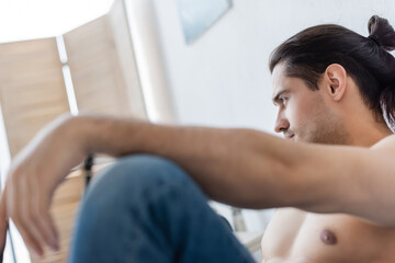 shirtless man in blurred jeans looking away at home.