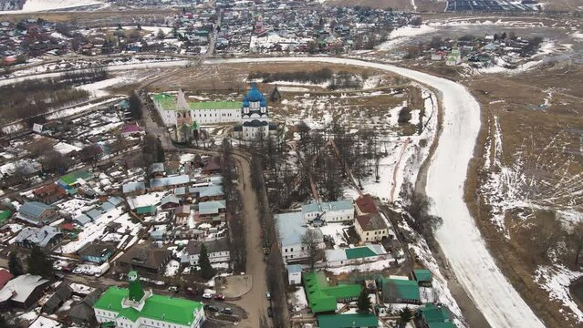 A long curved frozen river, the ice is melting, a small town is on the shore. Spring, snow melts, dry grass, flood and river flood. Day, cloudy weather, soft warm light. UHD 4K