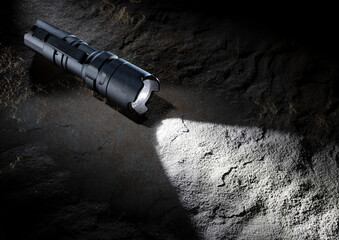 Survival flashlight that is illuminated and glowing on a rock in low light around