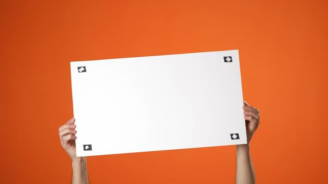 Hold in hands blank empty sign white big board tracking points for promotional content, pointing finger on place for text isolated orange background in studio. Copy space advertising area mock up