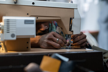 Medium close-up of unrecognizable fashion designer or tailor sitting at table using sewing machine to make new piece of clothing