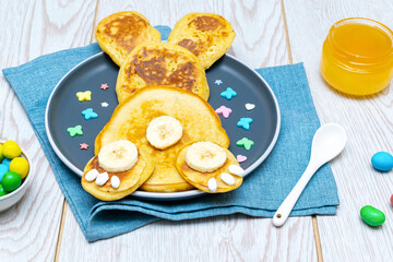 Easter funny creative healthy breakfast lunch food idea for kids, children.Bunny, rabbit made from pancakes,banana with honey,sweet candies,eggs on plate wooden table background.Top view Flat lay