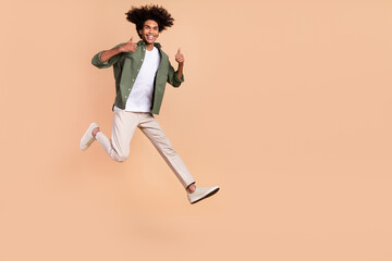 Fototapeta na wymiar Full length body size view of attractive cheerful guy jumping showing thumbup isolated over beige pastel color background