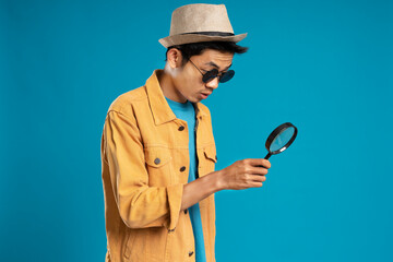 A young man wearing a jacket and hat amazed looking down with a magnifying glass © Zulfan