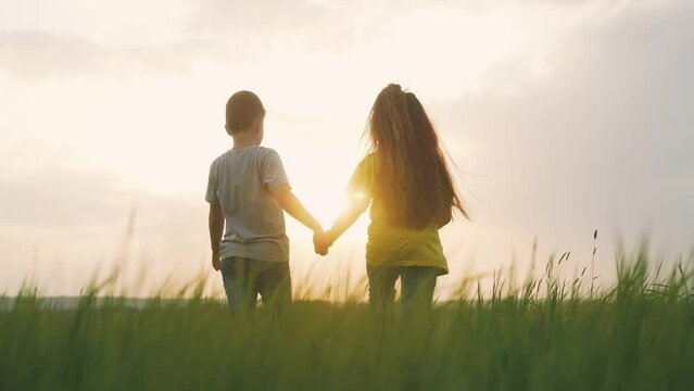 children walking a in the park. boy and friendship girl are holding hands walking on the grass in the park at sunset. happy family in nature outdoors. children holding hands at sunset happy family