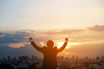 silhouette hand raised fist business man with sun lighting in morning. background city, success,...