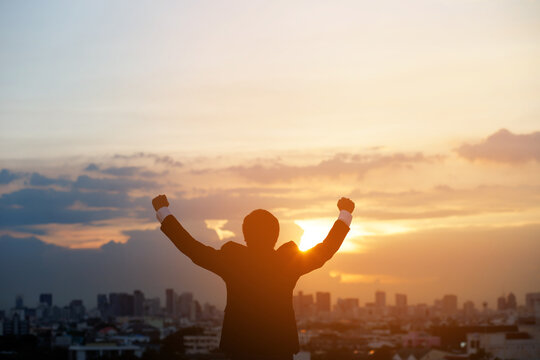 silhouette hand raised fist business man with sun lighting in morning. background city, success, grow up.