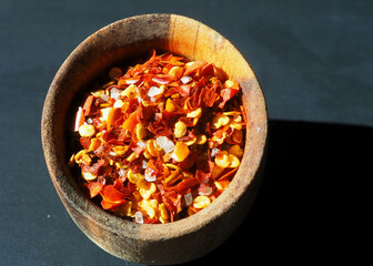 A mixture of cayenne pepper, red pepper and sea salt in a wooden bowl isolated on a black background. View from above. Spices concept