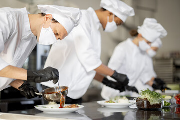 Multiracial group of cooks finishing main courses while working together in the kitchen. Cooks...
