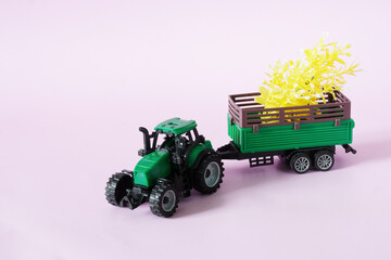 A green toy tractor is carrying yellow seedlings in a trailer. Spring planting and agricultural...