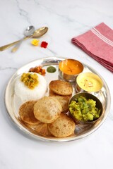 Indian vegetarian Thali or platter includes Aloo ki sabji, dal rice, Puri bhaji, Shrikhand or Srikhand, Aamras, papad, pickle, and chutney. Indian food is served in a Silverplate or thali. Copy Space.